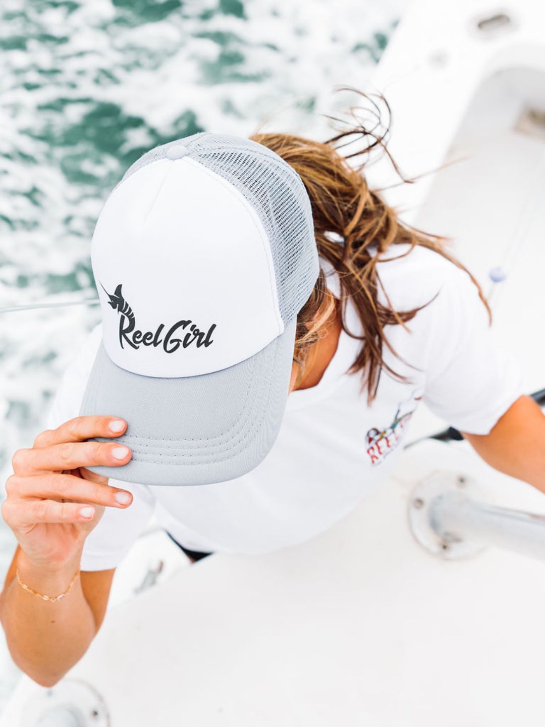 Person wearing a cap with 'Reel Girl' logo against a blurred water background