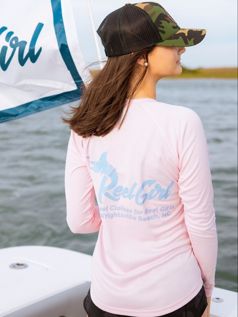 Woman on a boat wearing a pink 'Real Girl' shirt with a water background