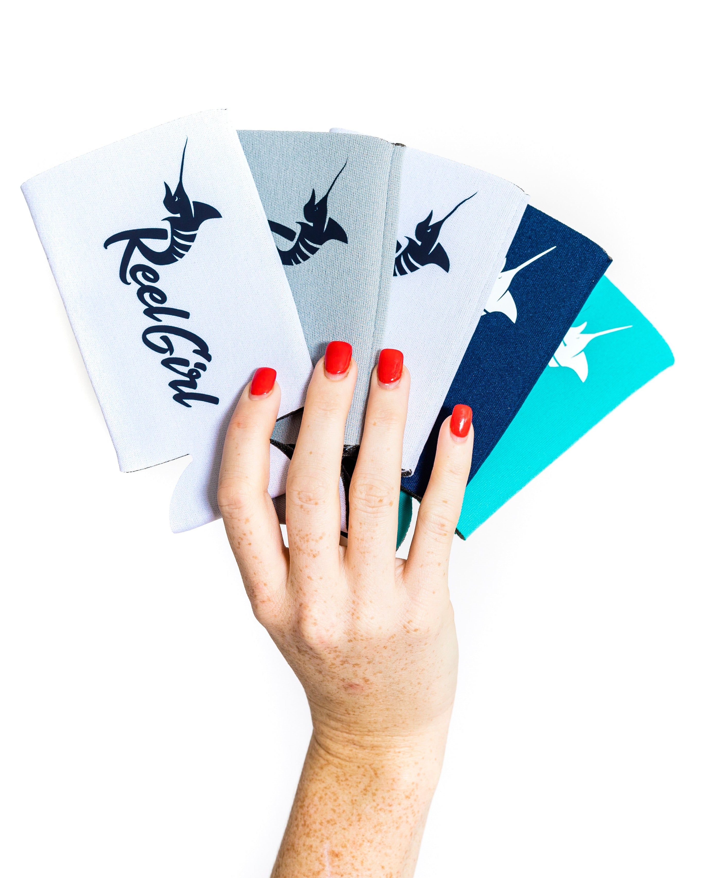 A hand holding three slim koozies in red, gray, and blue colors, with the 'Reel Girl' brand logo visible on each.